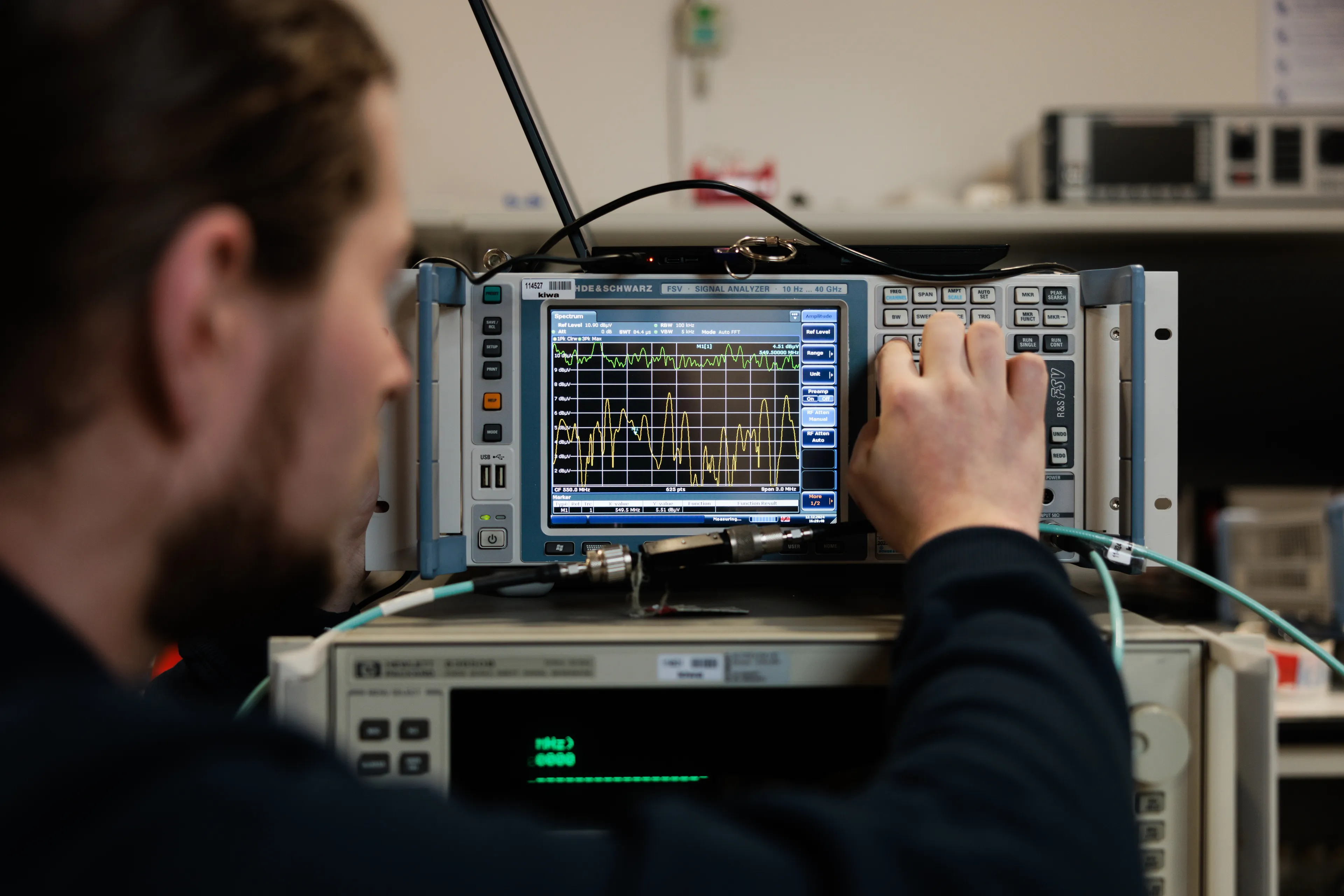 Technician adjusting a spectrum analyzer display in a laboratory with electronic test equipment