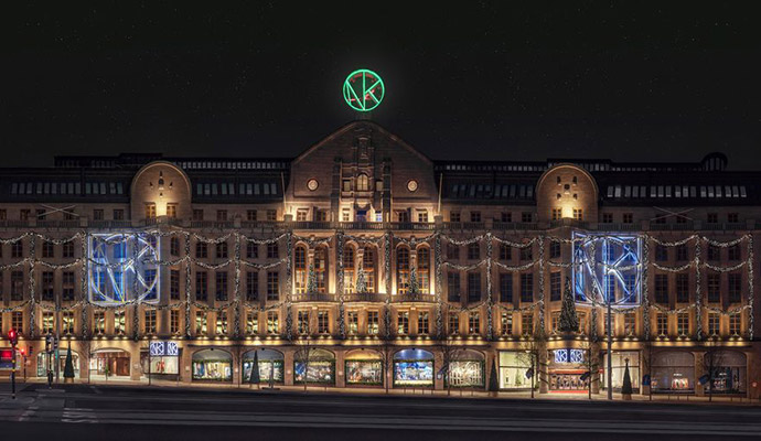 Varuhuset NK i Stockholm upplyst med dekorativa ljus och skyltar på fasaden under kvällen.