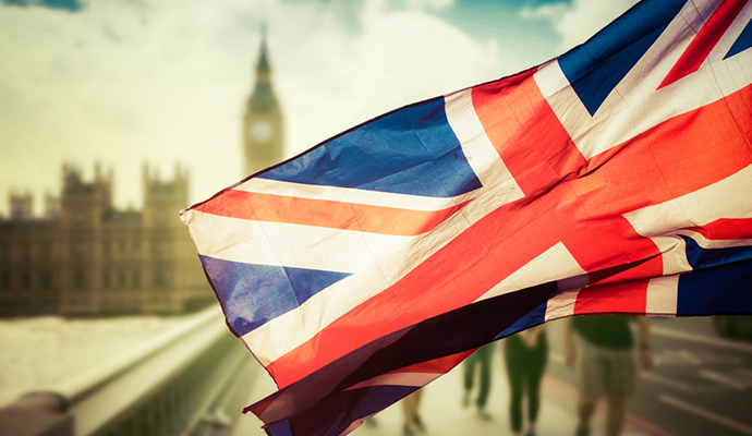 Union Jack-flagga vajar i vinden med Big Ben och Westminster Palace i bakgrunden under en solig dag.