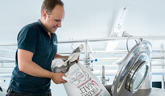 Man som häller en säck märkt "Vindsalt" i en industriell maskin.