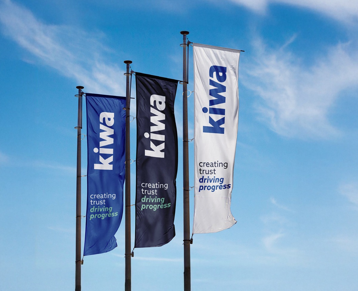 Three vertical flags displayed outdoors, featuring the Kiwa logo and the slogan "creating trust driving progress" against a blue sky with scattered clouds.
