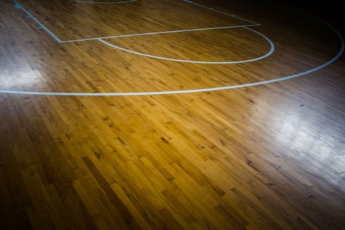 Basketbalveld met houten vloer en wit gemarkeerde lijnen.
