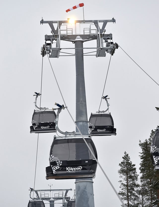 Skidlift med svarta gondoler och logotypen "Kläppen" på en grå stålkonstruktion mot en molnig himmel.