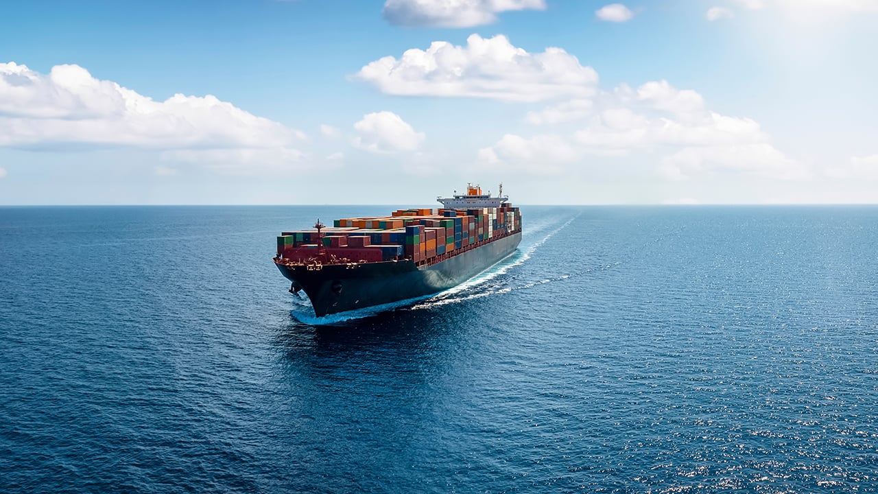 Ett stort containerfartyg som seglar på öppet hav under en klar blå himmel med vita moln.