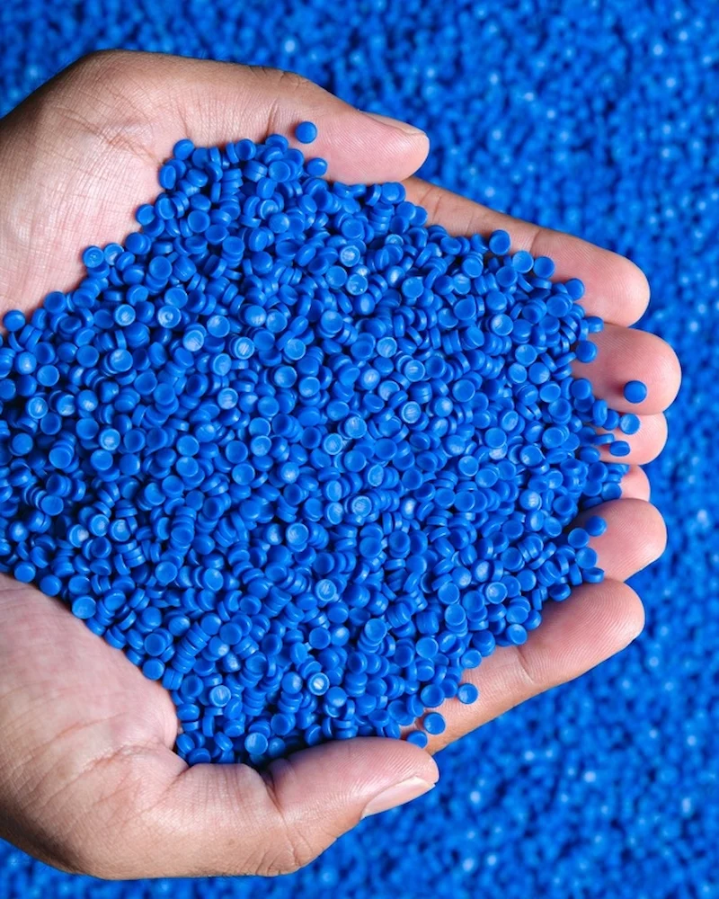 Hand holding bright blue plastic polymer pellets used in manufacturing