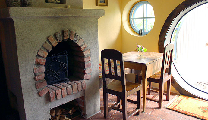 Inuti hobbithotellet med sina runda f&ouml;nster, &ouml;ppen spis och litet matbord med tv&aring; stolar och en b&auml;nk mot v&auml;ggen.