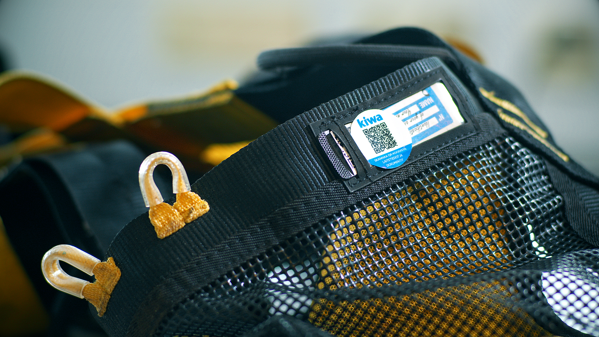 Close-up of a black mesh bag with yellow accents and a label featuring a QR code.