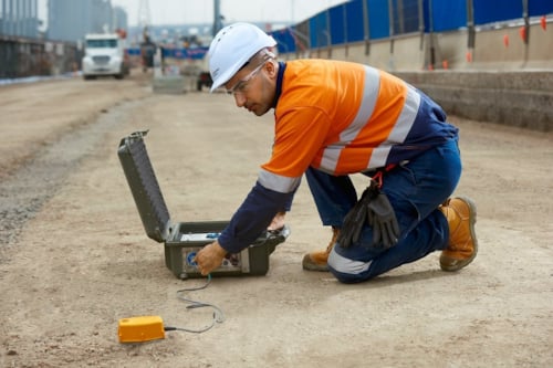 Kiwa auditor wearing a hard hat and safety gear, operating a device on a construction site