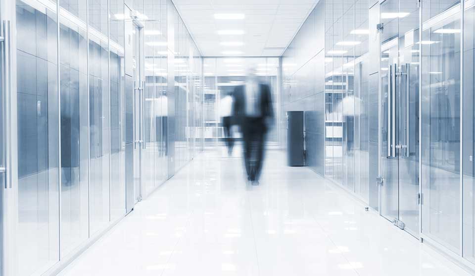 blurry image of a man in suit walking down a corridor in a glass building