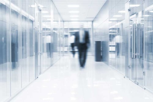 blurry image of a man in suit walking down a corridor in a glass building