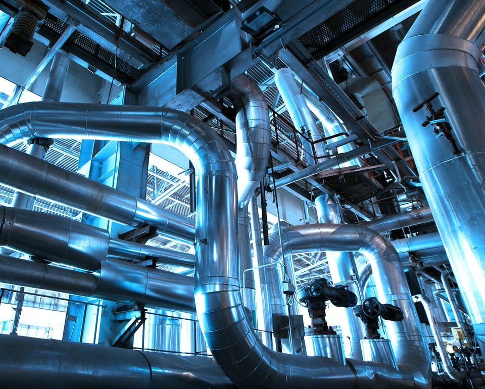 Industrial piping system with interconnected metal pipes and valves, showcasing complex engineering infrastructure within a facility, with a blue-tinted lighting