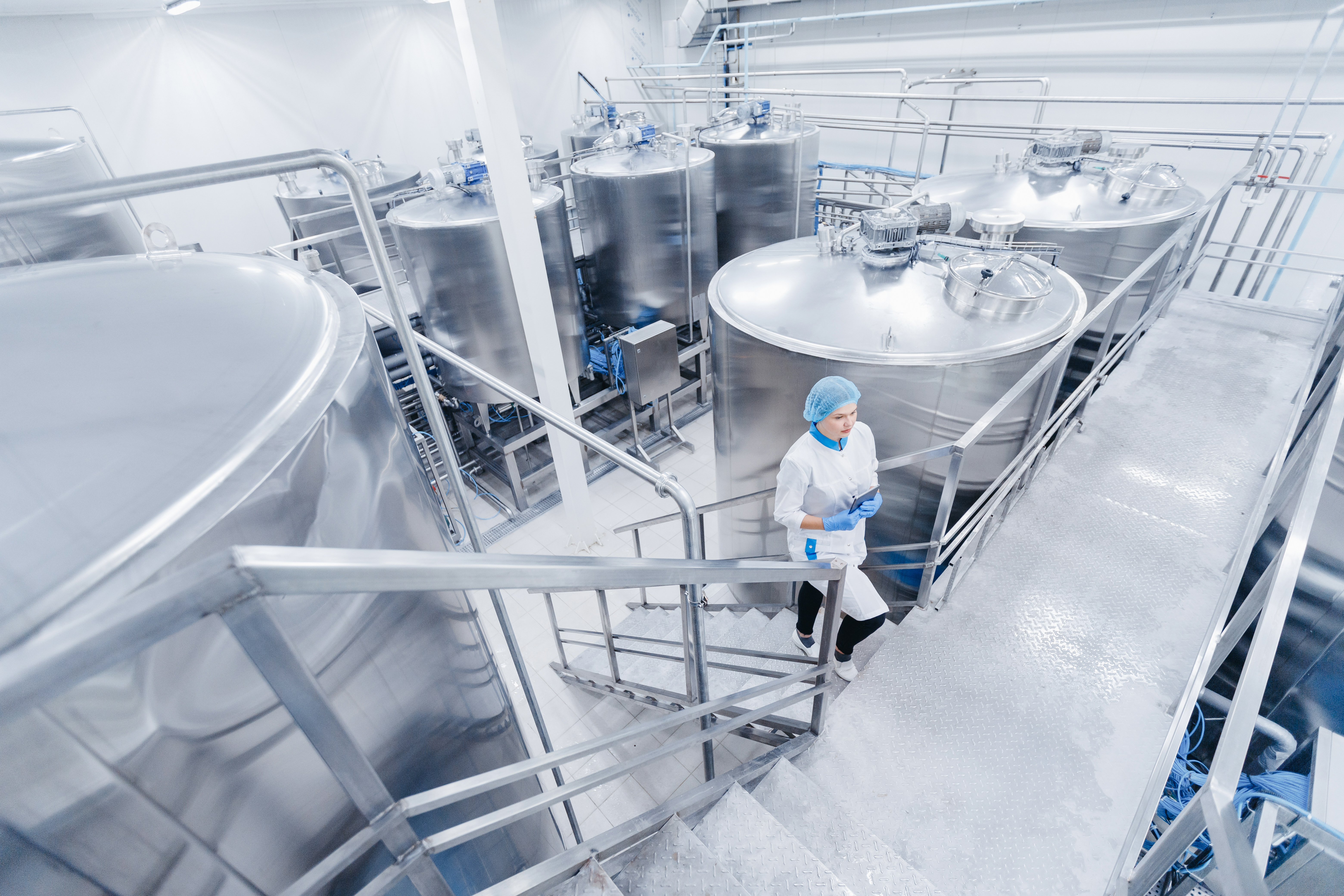 Kiwa inspector in a modern dairy processing facility with large stainless steel tanks, wearing protective clothing and hairnet