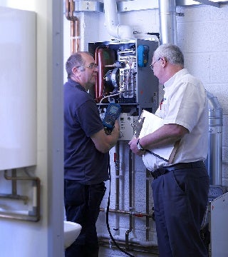 Two technicians inspecting and discussing a heating system in a utility room