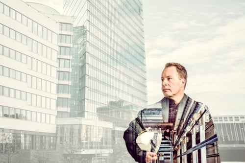Man holding a hard hat with a transparent architecture overlay, showcasing a cityscape featuring tall office buildings, reflecting modern urban development and construction themes