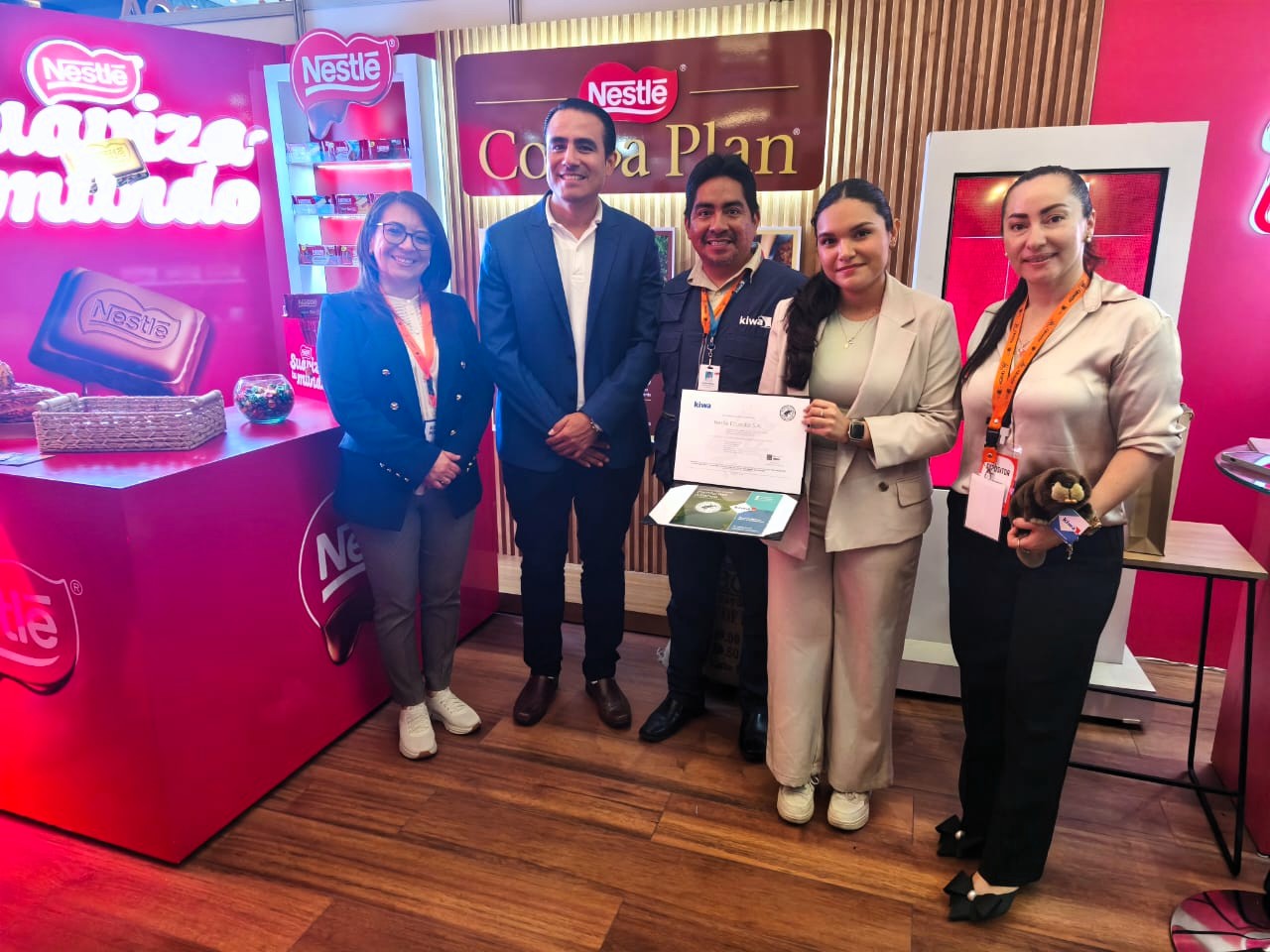 Group of people posing with a certificate at a Nestlé event booth showcasing the Nestlé Cocoa Plan, surrounded by branded displays and products