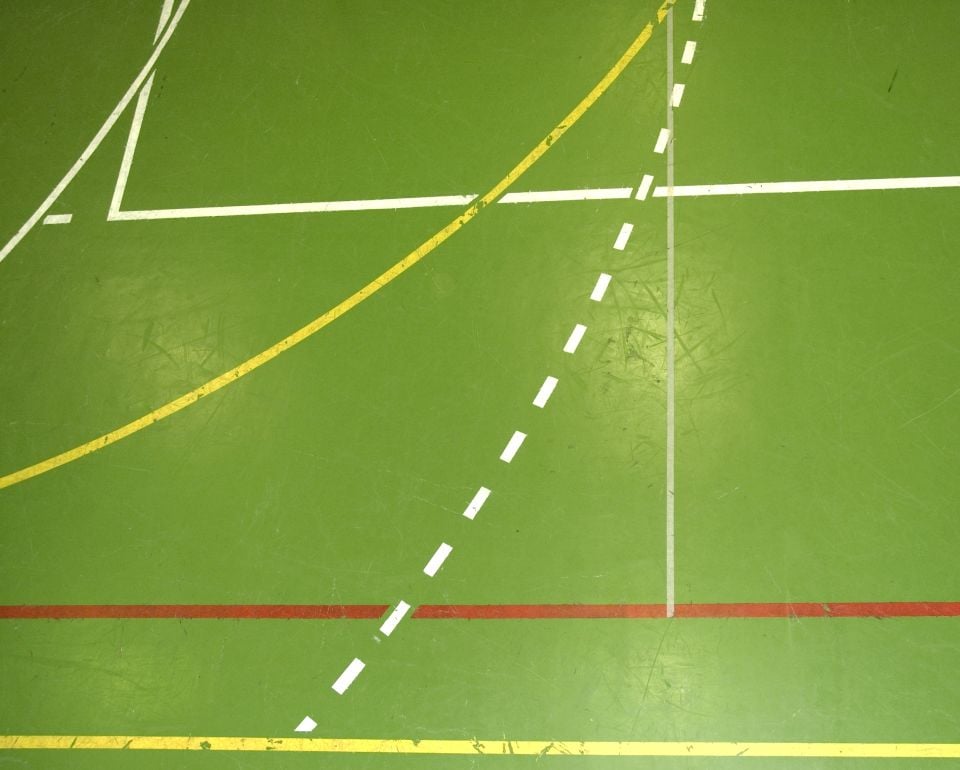 Groene sportvloer met witte, gele en rode lijnen voor speelvelden.