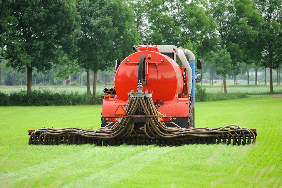 Rode mestinjecteurmachine met meerdere slangen op een groen grasveld