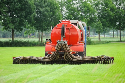 Rode mestinjecteurmachine met meerdere slangen op een groen grasveld