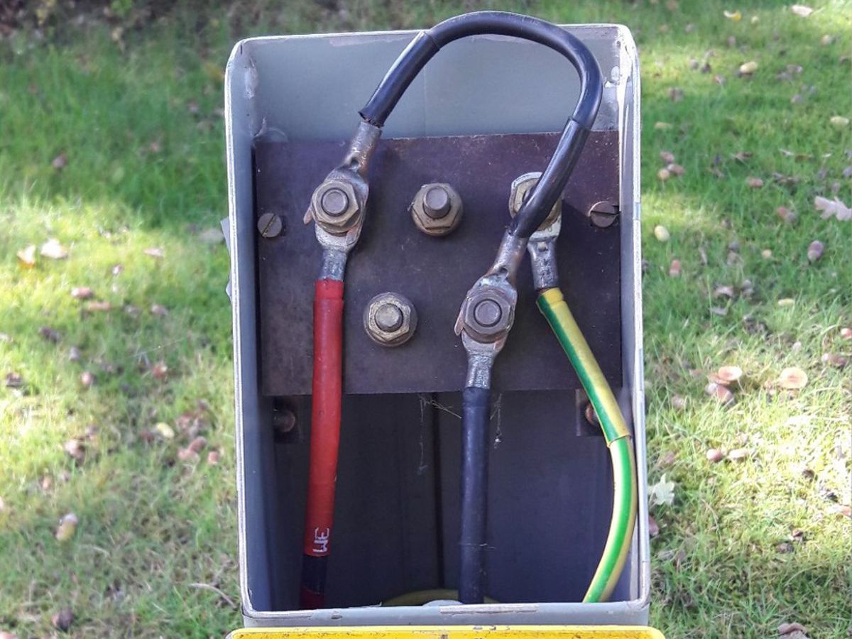 Open elektrische aansluitkast met drie dikke kabels en boutverbindingen in een groene buitenomgeving