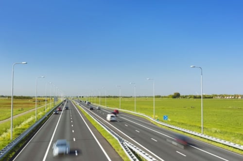 Snelweg met meerdere rijstroken in een open landschap onder een heldere blauwe hemel.