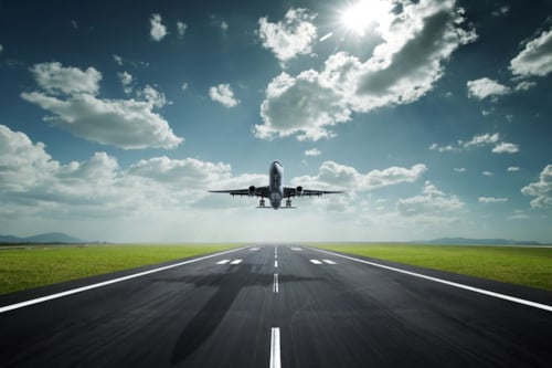 Een vliegtuig dat opstijgt vanaf een lege landingsbaan onder een blauwe lucht met wolken.