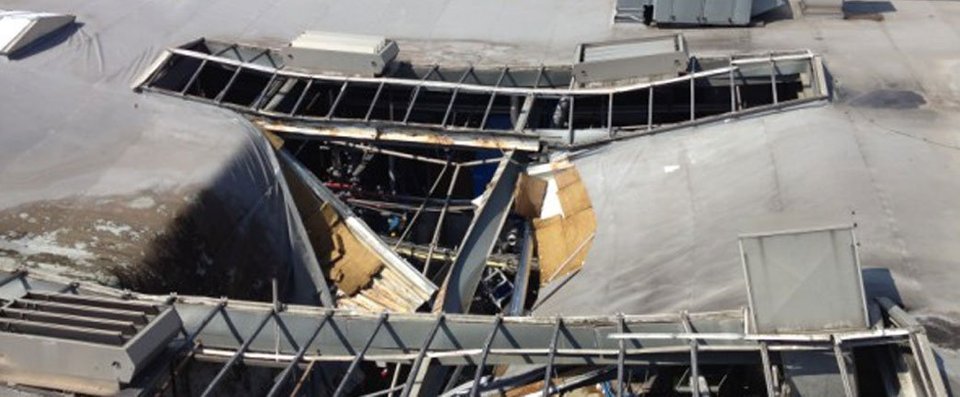 Schade aan een gebouwenstructuur, met een groot gat in het dak en blootgestelde metalen balken.