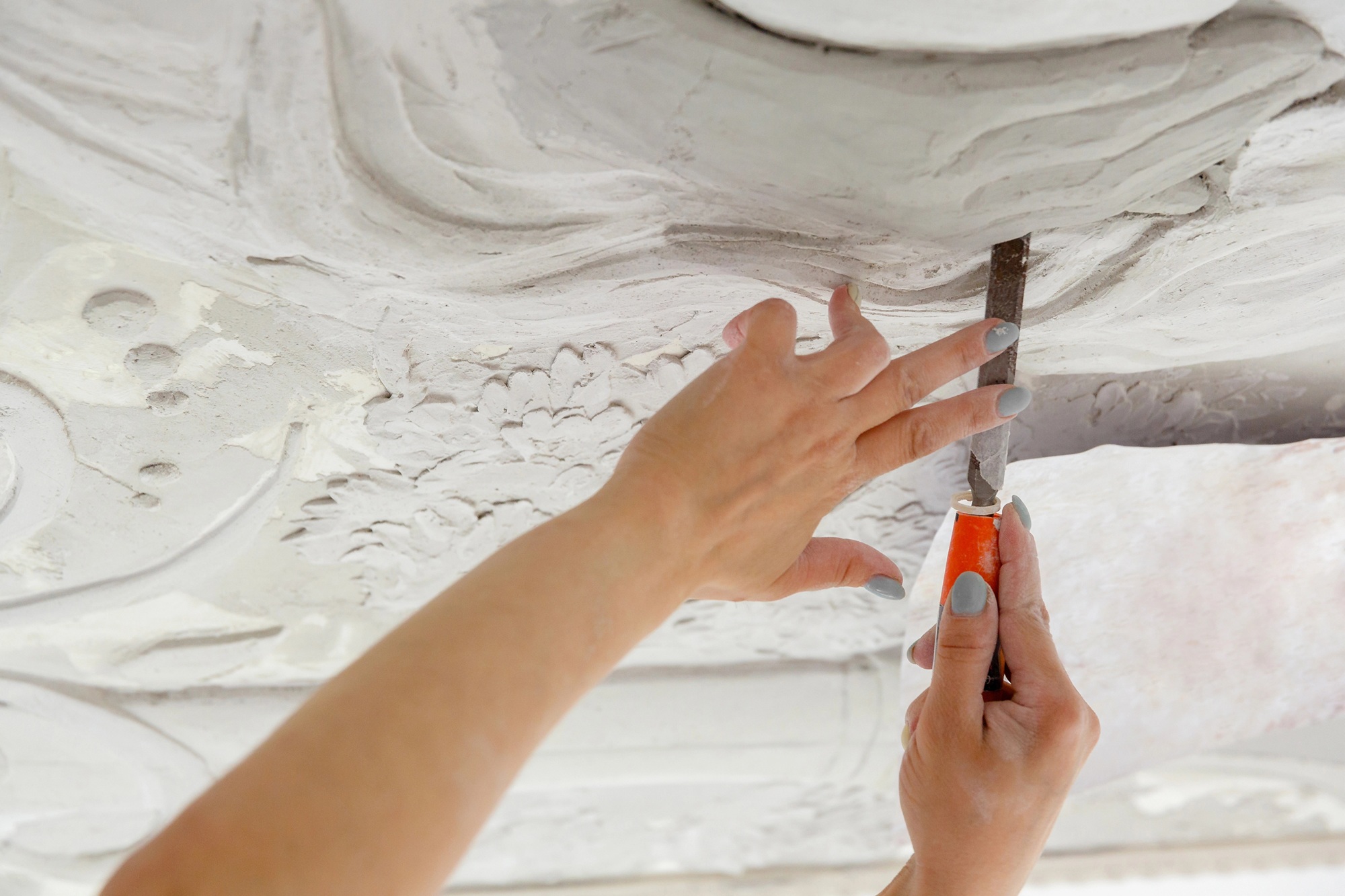 Handen met een beitel die een gedetailleerde decoratie in een wit oppervlak bewerken.