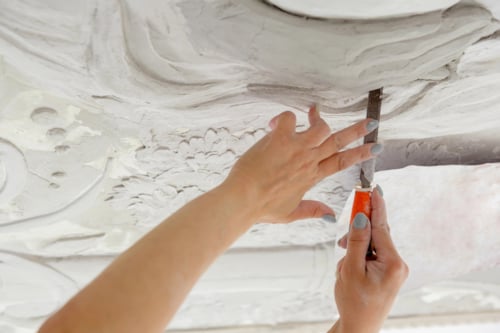 Handen met een beitel die een gedetailleerde decoratie in een wit oppervlak bewerken.