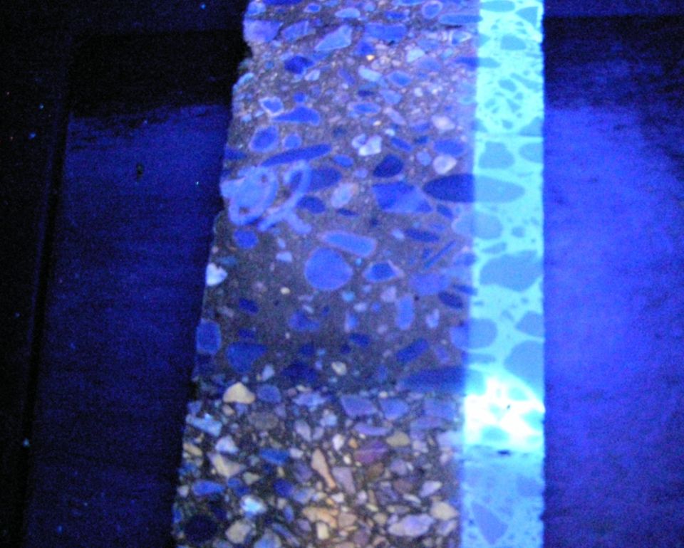 Een close-up van een asfalt oppervlak onder UV-licht, met een duidelijk contrast zichtbaar tussen verschillende teer en asfalt.