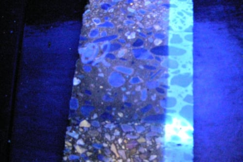 Een close-up van een asfalt oppervlak onder UV-licht, met een duidelijk contrast zichtbaar tussen verschillende teer en asfalt.