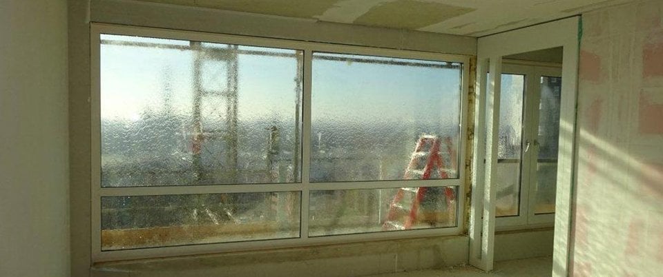 Uitzicht vanuit een gebouw met grote ramen, een vervaagde bouwkraan en een rode ladder zichtbaar buiten.