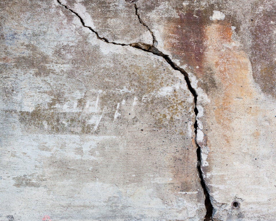 Betonnen oppervlak met een grote barst en verweerde plekken.