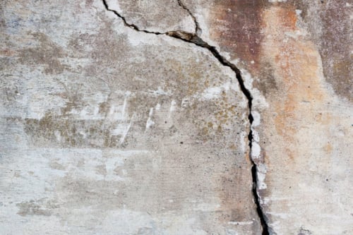 Betonnen oppervlak met een grote barst en verweerde plekken.