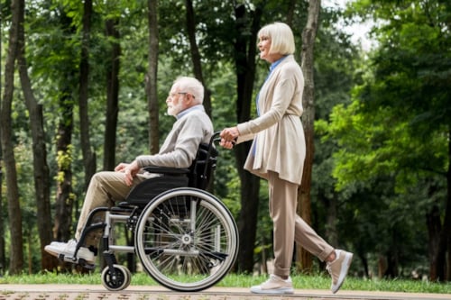 Oudere man in een rolstoel wordt voortgeduwd door een vrouw in een park