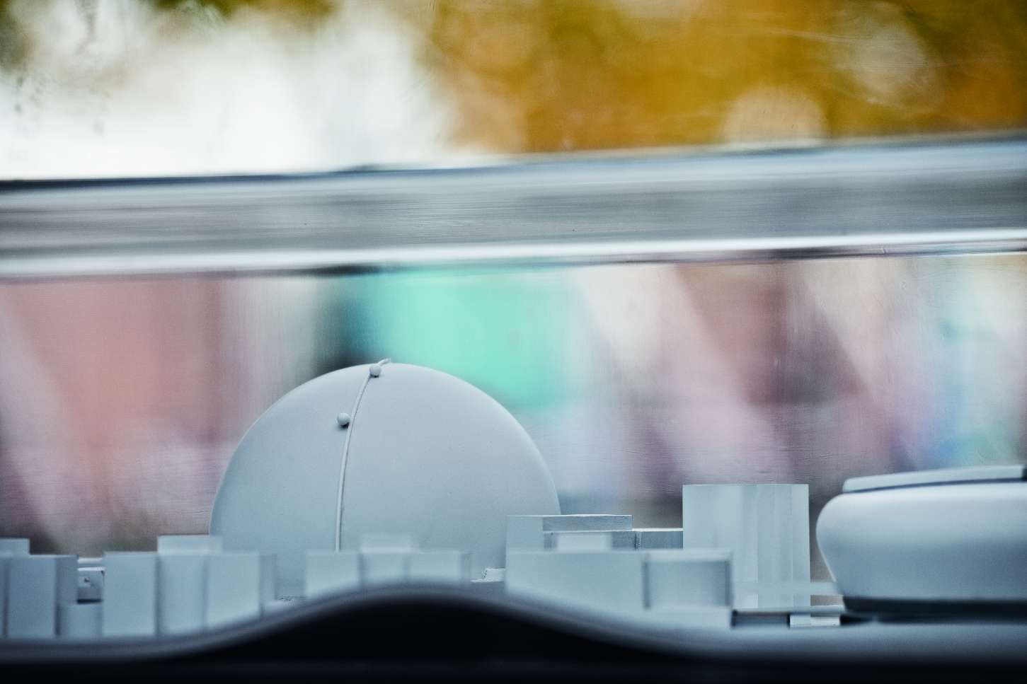 Arkitekturmodell som visar en stadsplan med en vit kupolformad byggnad och omgivande strukturer, suddigt landskap i bakgrunden.