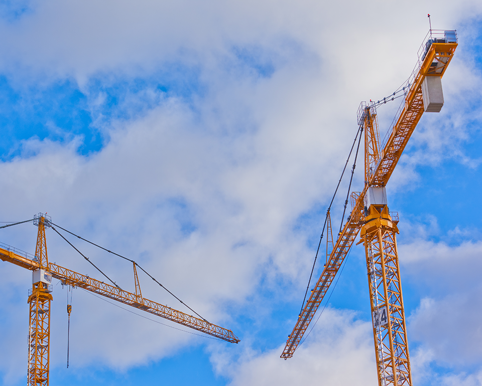 Två gula byggkranar mot en blå himmel med vita moln.