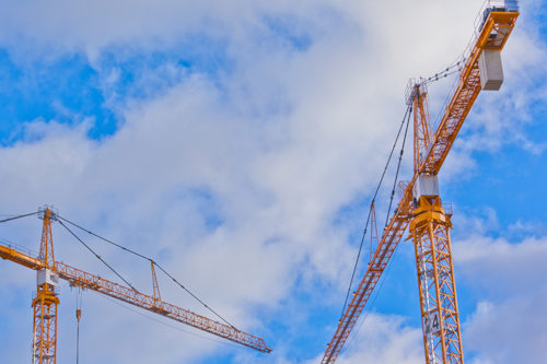 Två gula byggkranar mot en blå himmel med vita moln.