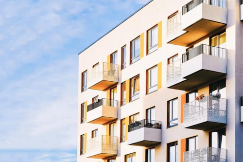 Flerfamiljsbostad med flera balkonger och blå himmel.
