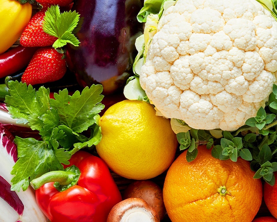 Närbild av en grupp färska frukter och grönsaker, inklusive blomkål, citroner, apelsin, jordgubbar, paprika, aubergine och örter.