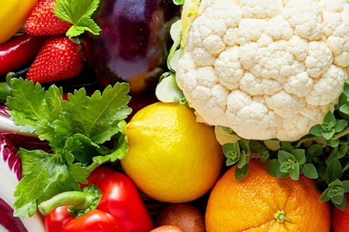 Närbild av en grupp färska frukter och grönsaker, inklusive blomkål, citroner, apelsin, jordgubbar, paprika, aubergine och örter.