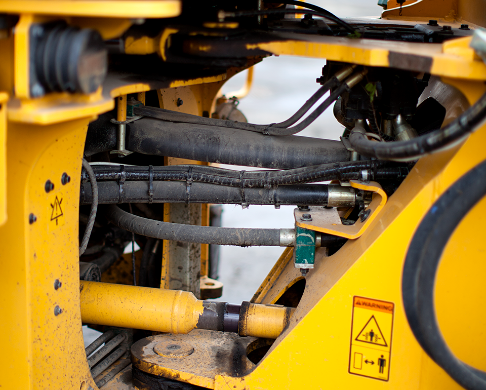 Hydraulslangar och andra rörledningar på en gul maskin. 