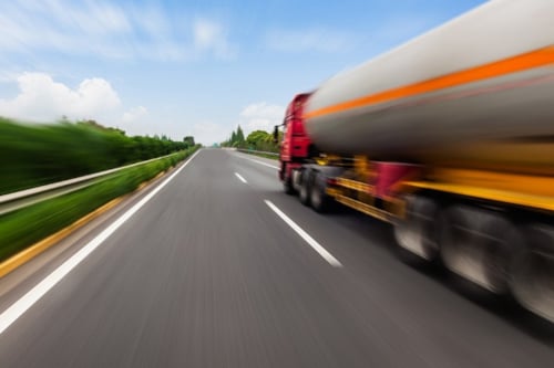 En tankbil susar fram på en rak landsväg, som sträcker sig långt fram mot horisonten.