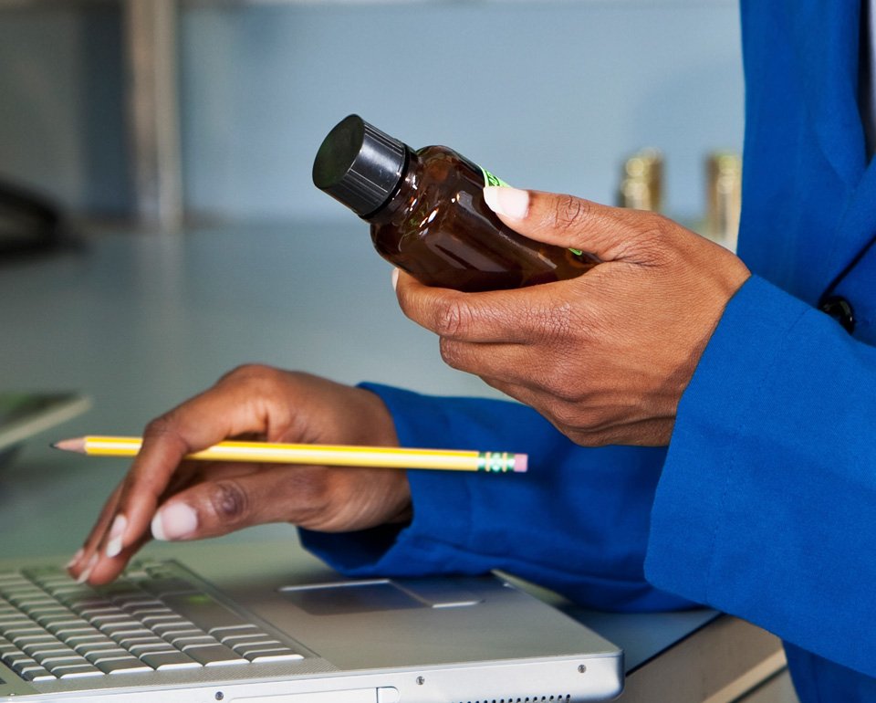 Kvinna håller i en brun flaska och en gul penna medan hon skriver på en bärbar dator.