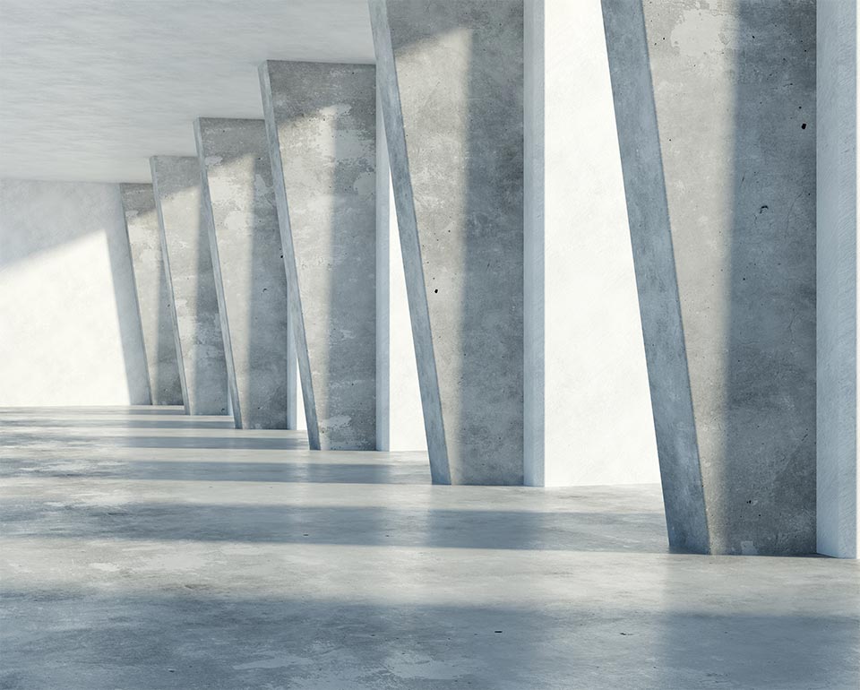 Betongväggar och pelare i en ljus, minimalistisk byggnad med solljus som skapar skuggor på golvet.
