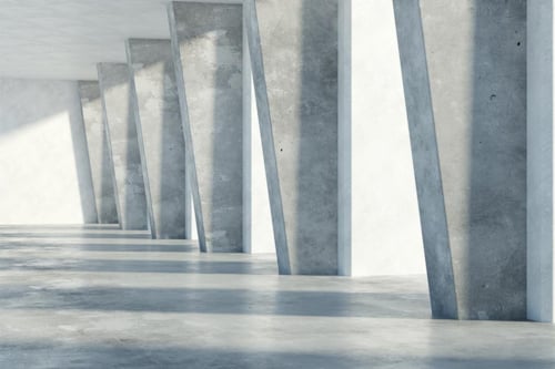 Betongväggar och pelare i en ljus, minimalistisk byggnad med solljus som skapar skuggor på golvet.