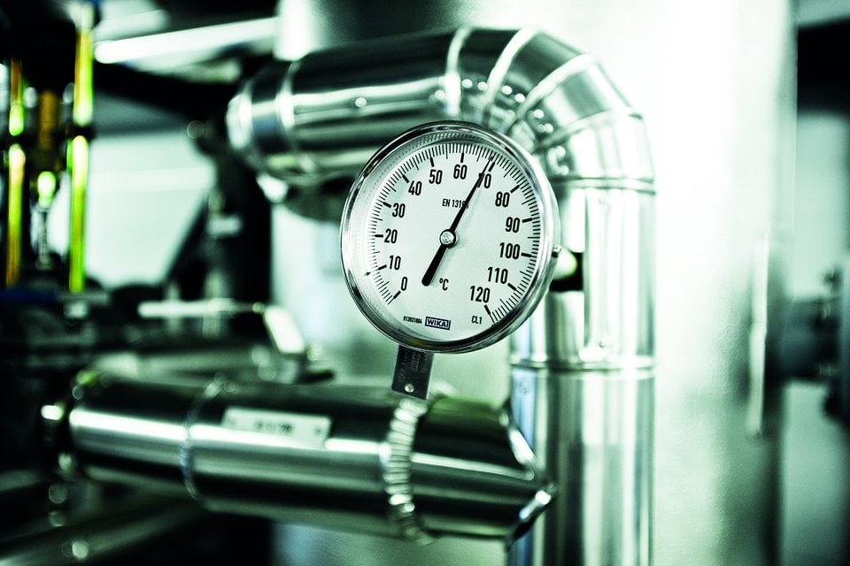 Manometer som mäter tryck, omgiven av metallrör i en industriell miljö.