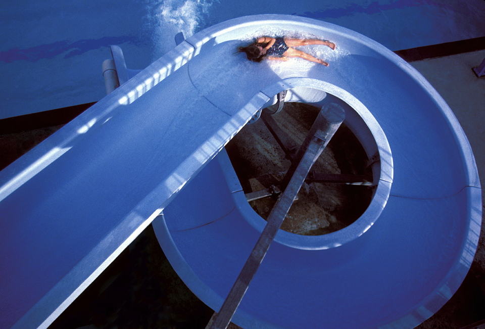 En person åker i en lång blå vattenrutschbana som skruvar sig nästan 360 grader.