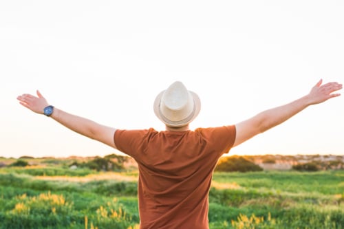 man standing in a filed with open arms