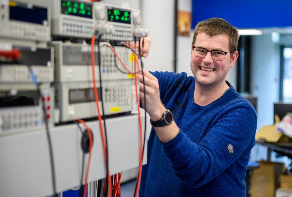 Kiwa technician Edwin Verweij, smiling in blue sweater working with electronic equipment in a laboratory setting