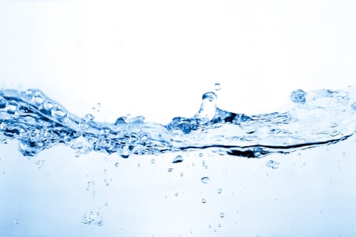 Klar vattenskvätt mot vit bakgrund, med synliga bubblor och rörelse i v